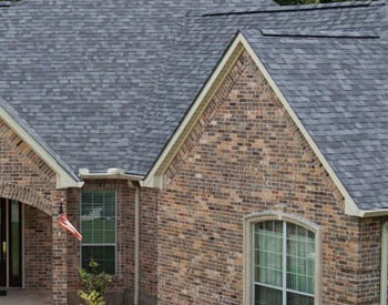 Front view of a large residential home with brown brick siding and gray Malarkey shingles